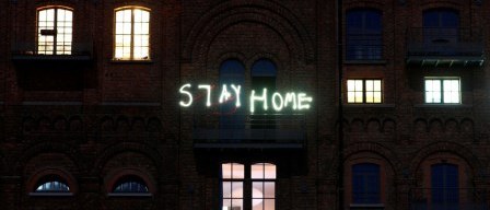 Wohnhaus mit Leuchtschrift "Stay home"
                  am Balkon