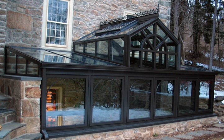 Angebautes Grubengew�chshaus in Schwarz
                          als Erweiterung eines Hauses an eine rohe
                          Steinmauer - sehr energieeffizient.