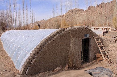 Der Bau des Grubengew�chshauses in
                            Ladakh, Nord-Indien: Die W�nde sind mit Lehm
                            verputzt, die Plastikplane ist in form eines
                            Halb-U mit einer Steinreihe befestigt