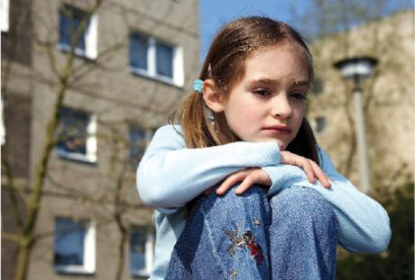 Ein Mädchen sitzt vor einem traurigen Wohnblock