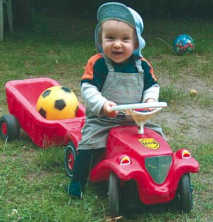 Bub lenkt Kinderauto mit Anhänger mit Ball