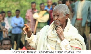 Redner mit
                          Hacken und Schaufeln an einer Dorfversammlung
                          02